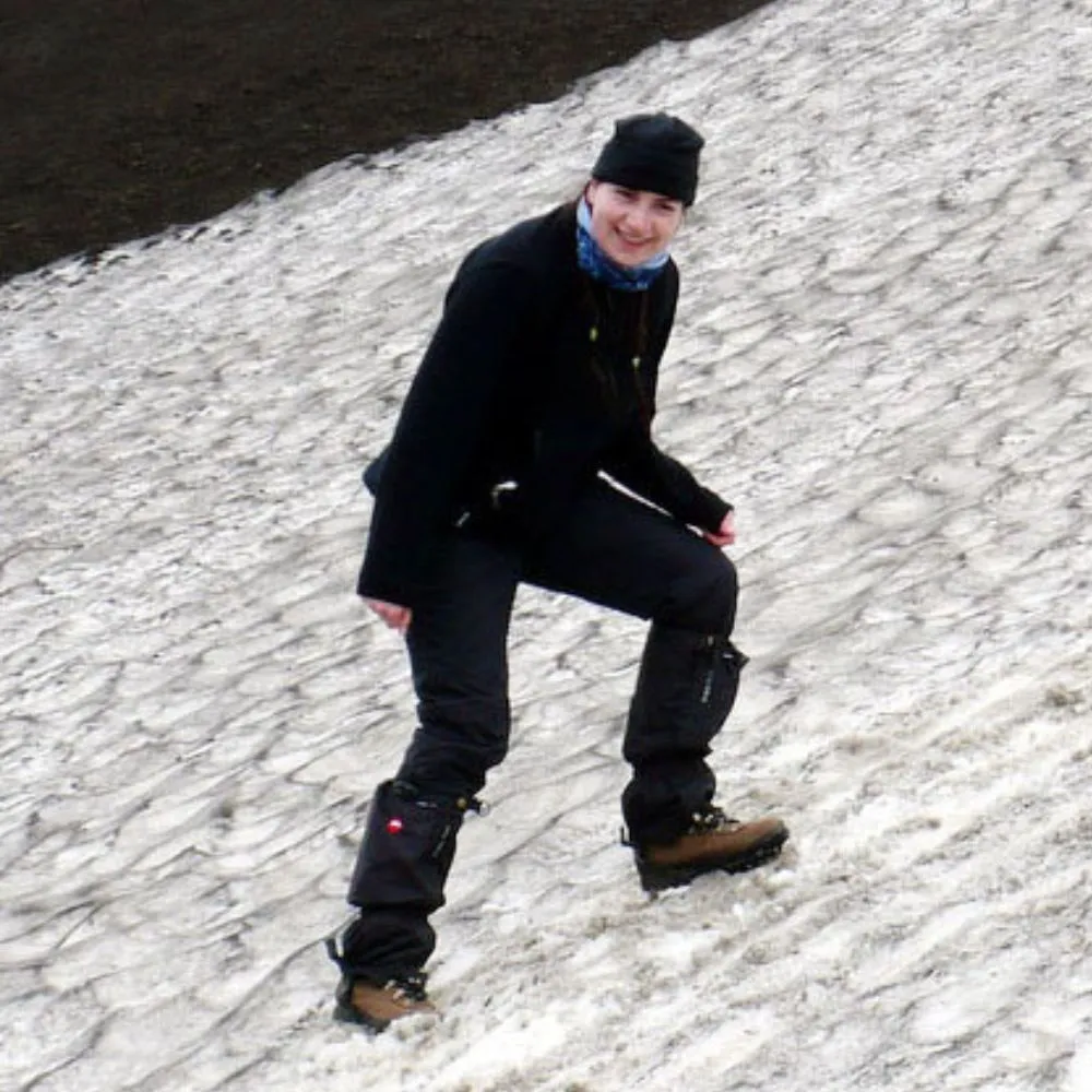 Person in hiking gear smiling while standing on a snowy hillside.