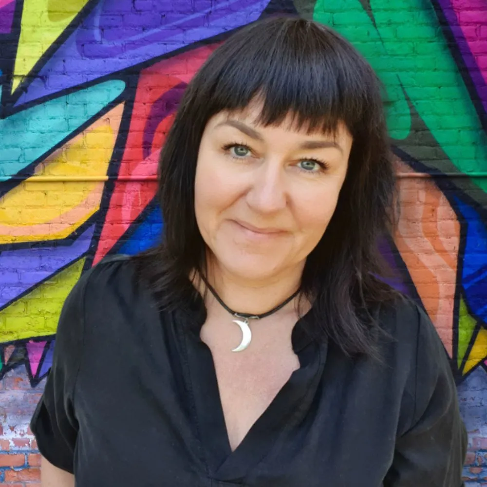 Person with dark hair smiling in front of a colourful mural.