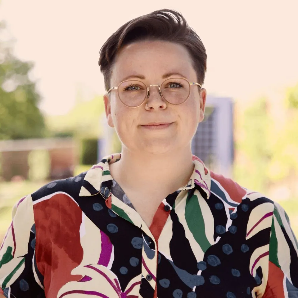 Person with short hair, glasses, and a colourful patterned shirt outdoors.