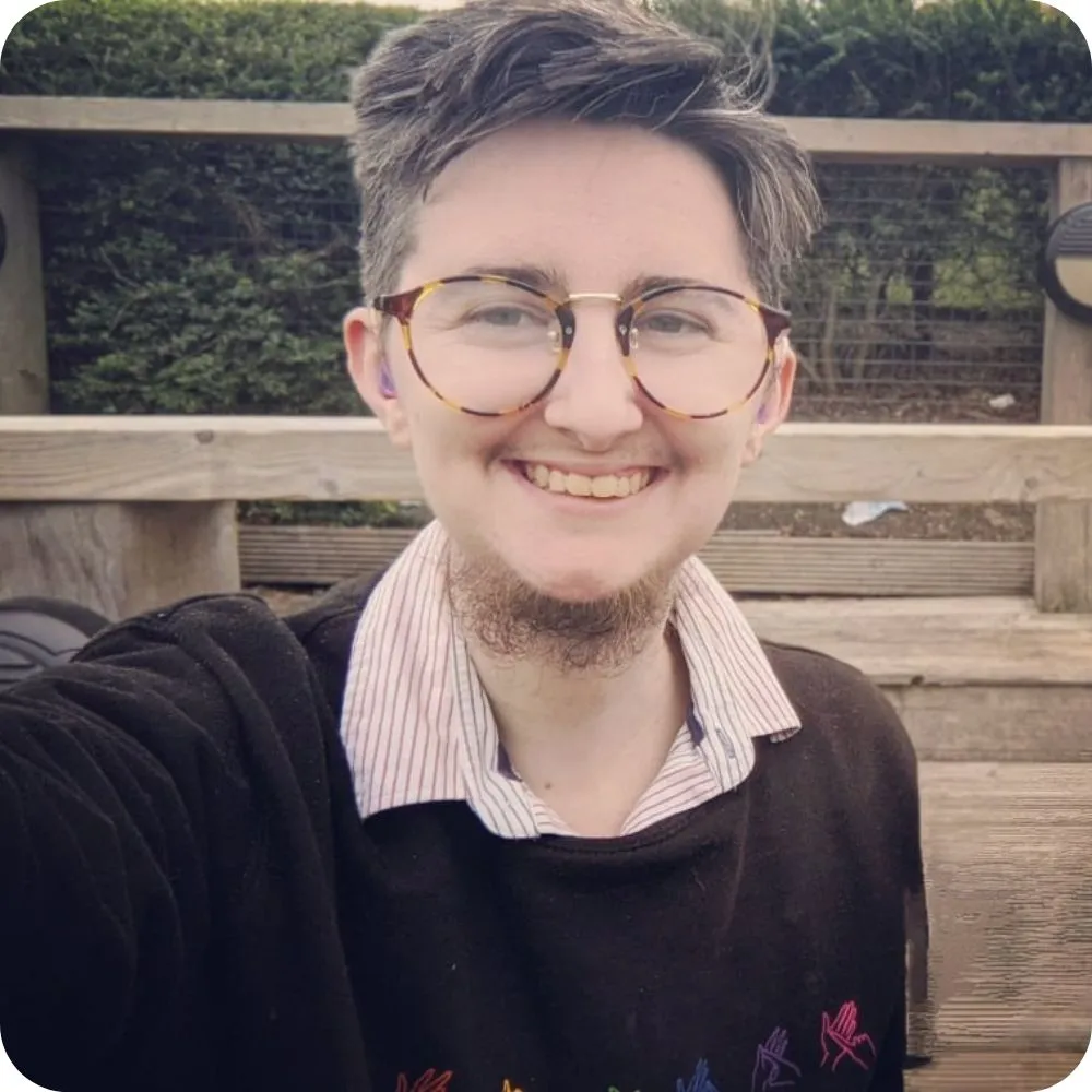 Smiling person with glasses and short hair taking an outdoor selfie.