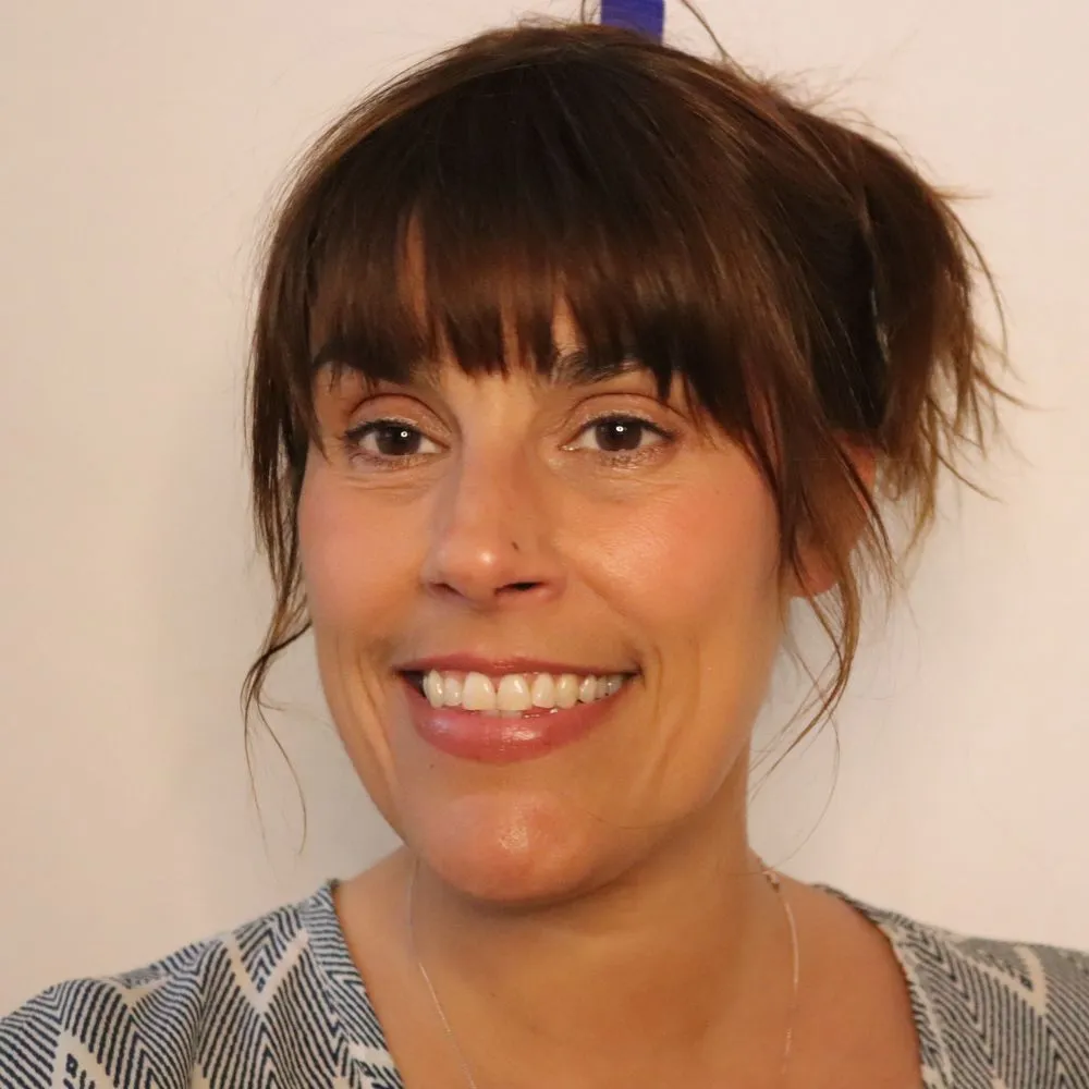 Smiling person with dark hair and bangs against a plain background.