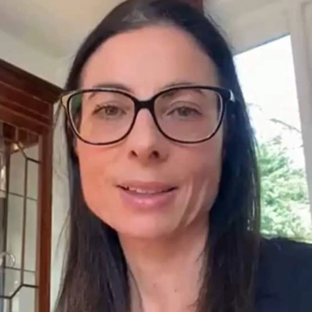 Person with long dark hair and glasses looking at the camera indoors.