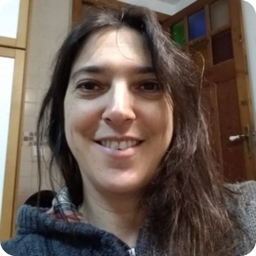 Smiling person with long dark hair wearing a grey hoodie indoors.