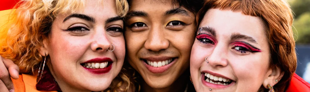 Three smiling young adults of diverse backgrounds pose closely together, celebrating friendship, individuality, and inclusion.