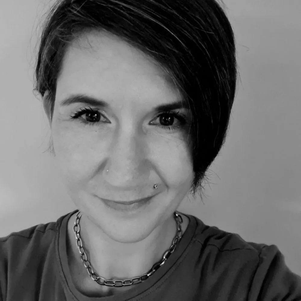 Black-and-white portrait of a smiling person with short dark hair and nose piercings.
