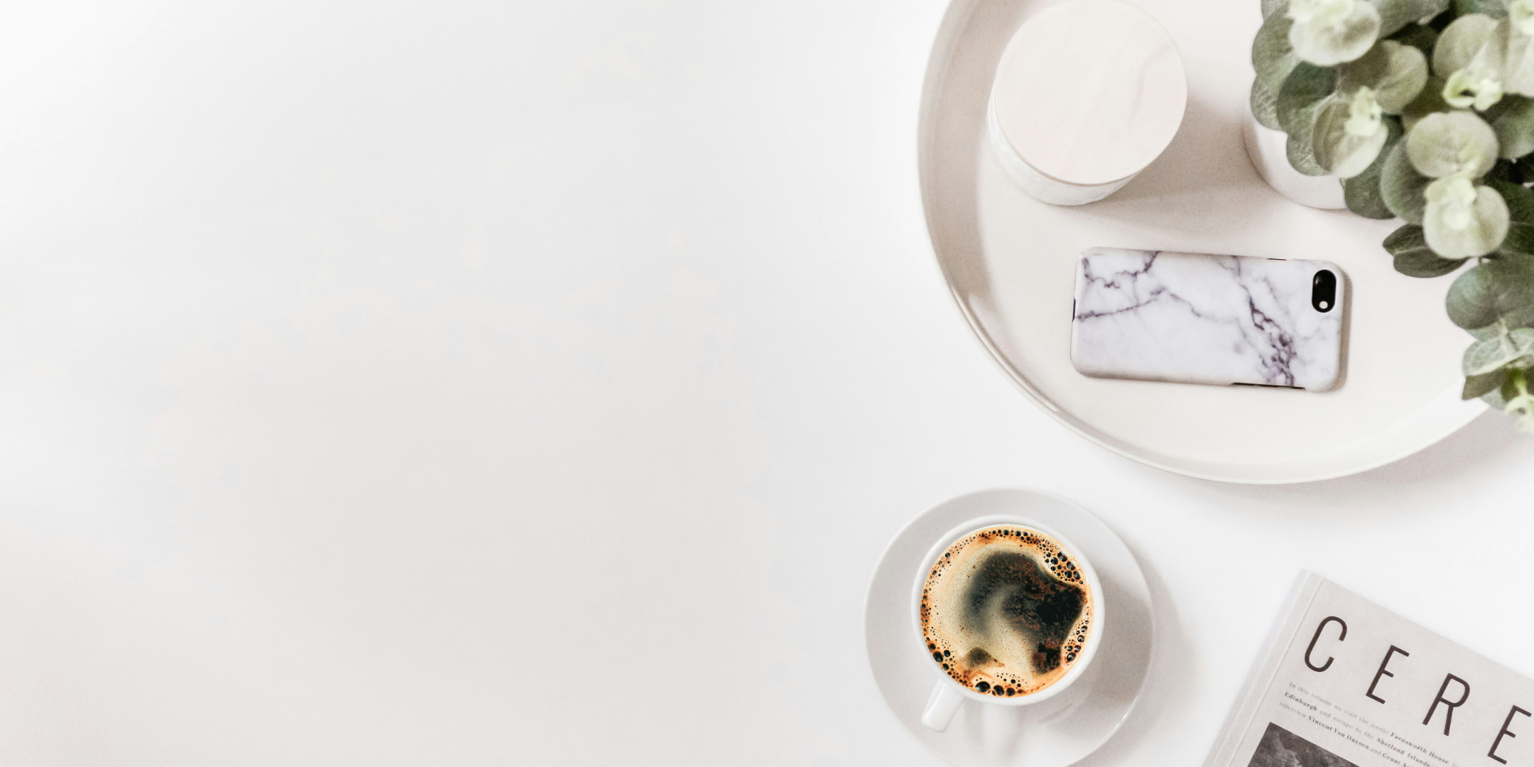 Minimal overhead workspace with a cup of coffee, smartphone, small plant and magazine arranged on a white surface with ample copy space.