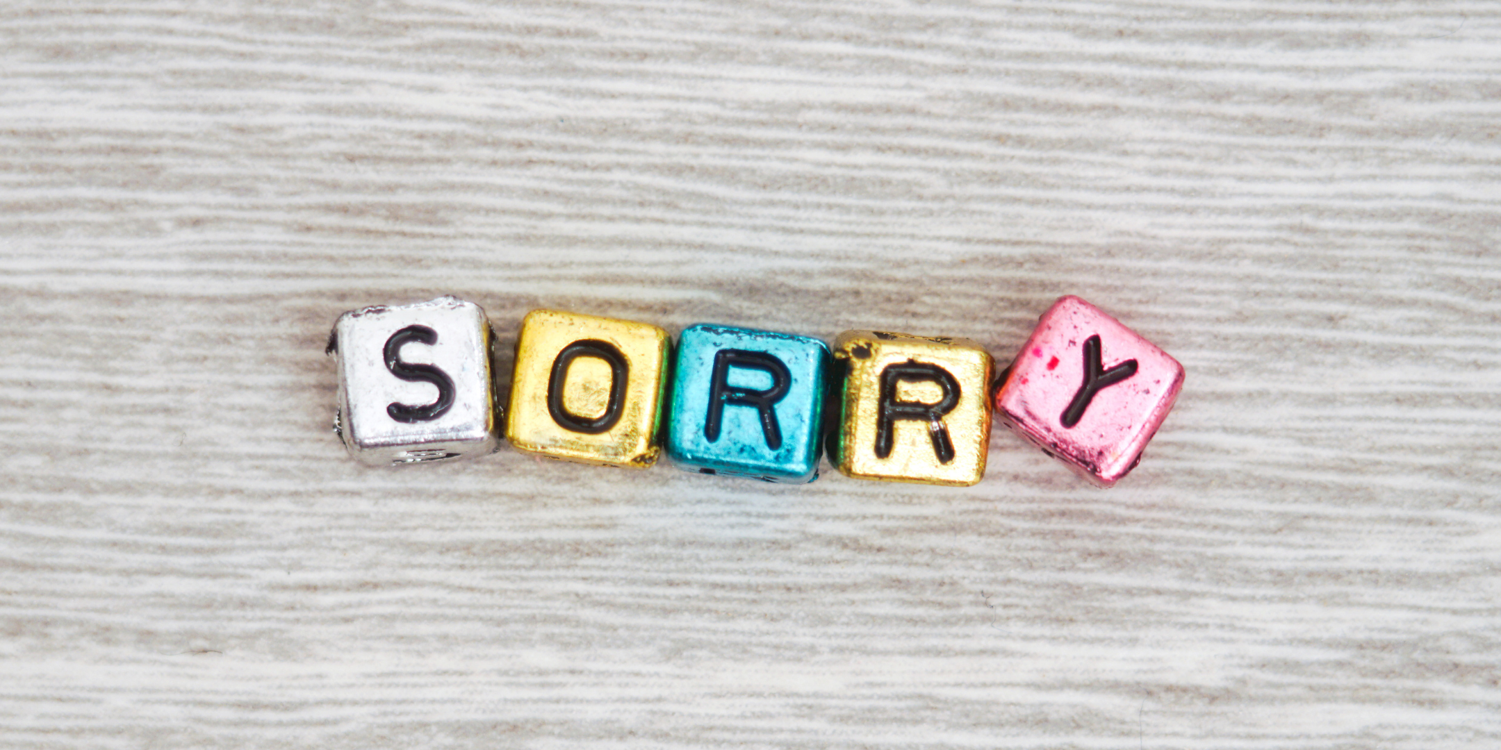Wooden letter blocks spelling "SORRY" on a wooden surface.