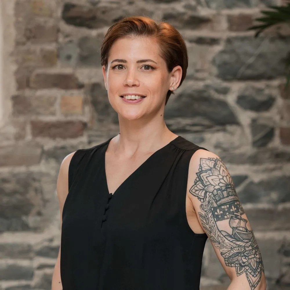 Person with short auburn hair and a tattooed arm wearing a sleeveless black top.