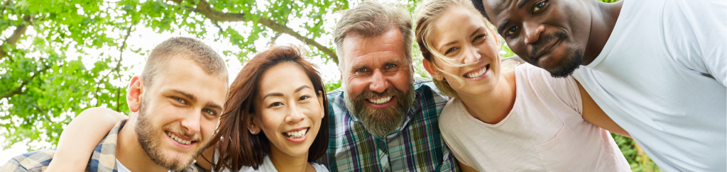 A diverse group of adults smiling together outdoors, representing connection, belonging, and community support.