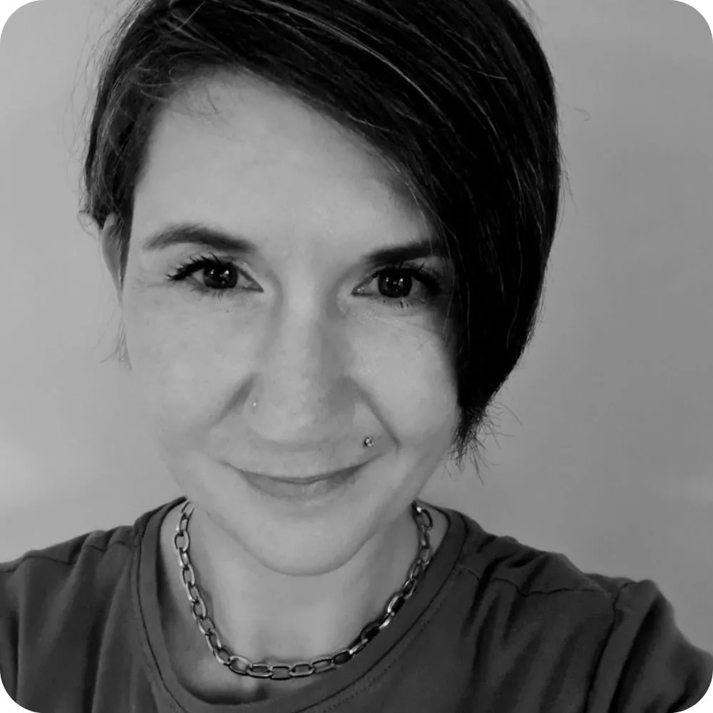 Black-and-white portrait of a smiling person with short dark hair and nose piercings.