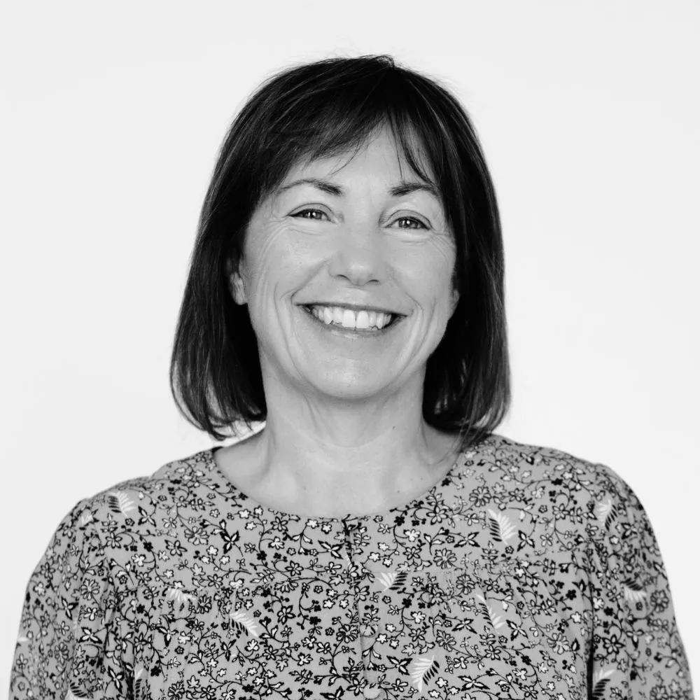 Black-and-white portrait of a smiling person with shoulder-length dark hair wearing a floral blouse.