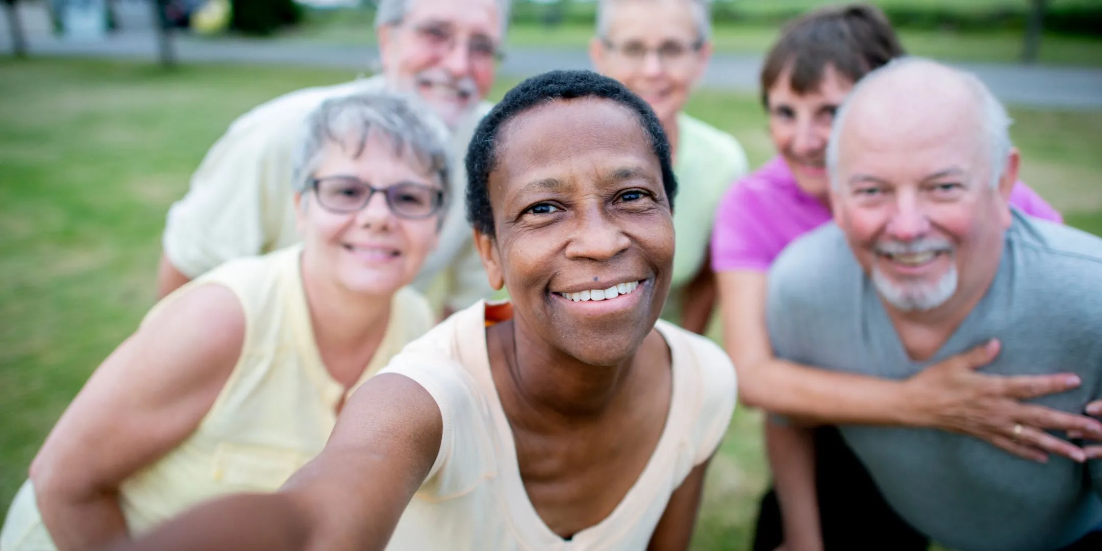 Diverse group of older adults smiling together for a cheerful outdoor group selfie.