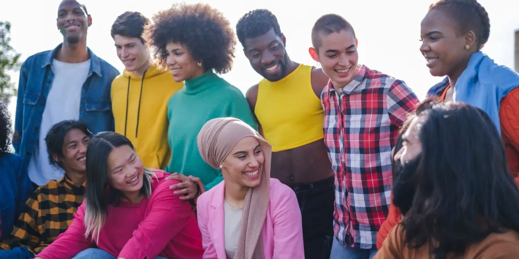 A diverse group of people smile and chat together outdoors, representing friendship, inclusion, and a welcoming community.