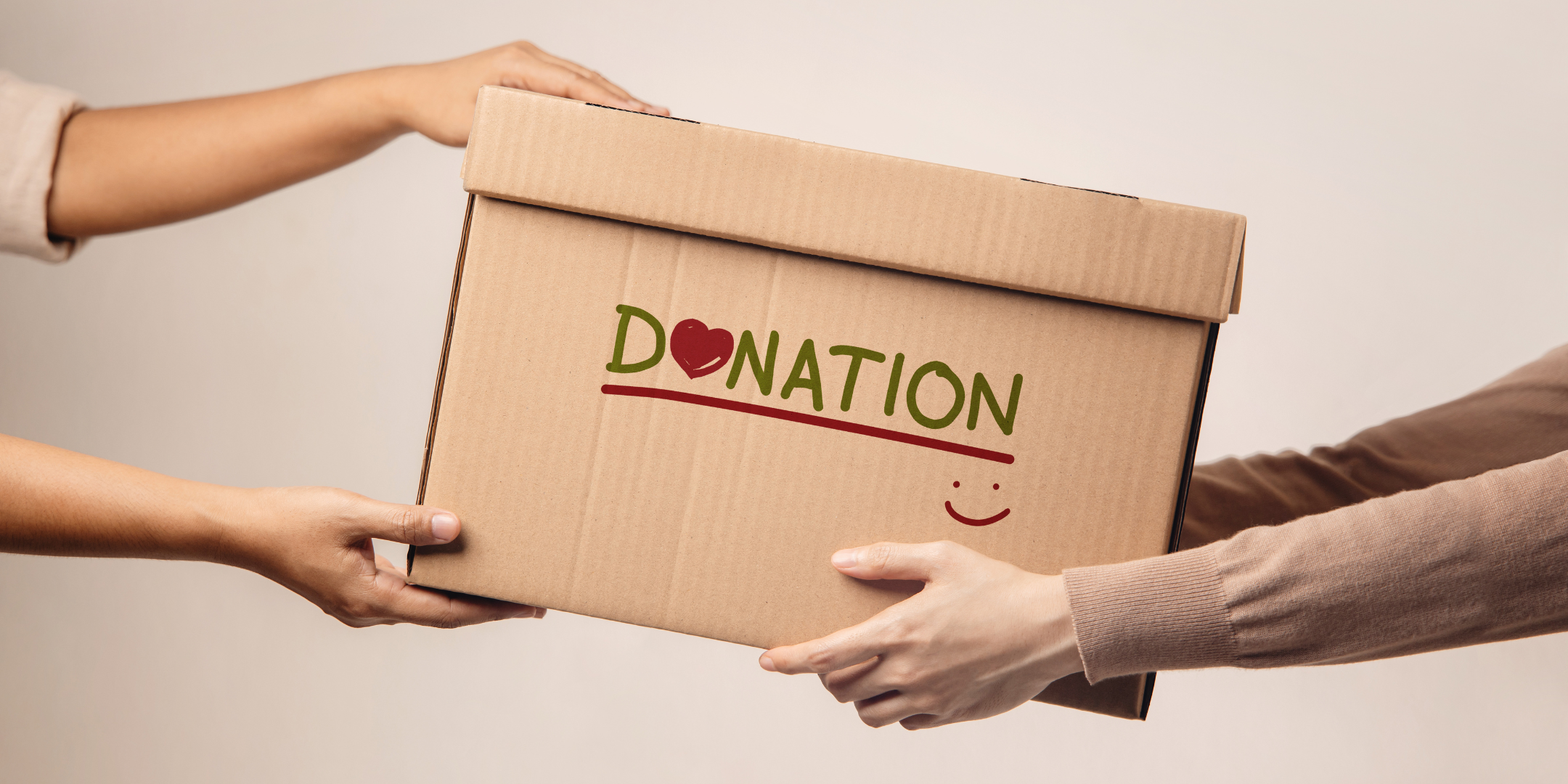 Several people pass a cardboard donation box between them, decorated with the word “DONATION,” a heart, and a smiling face.